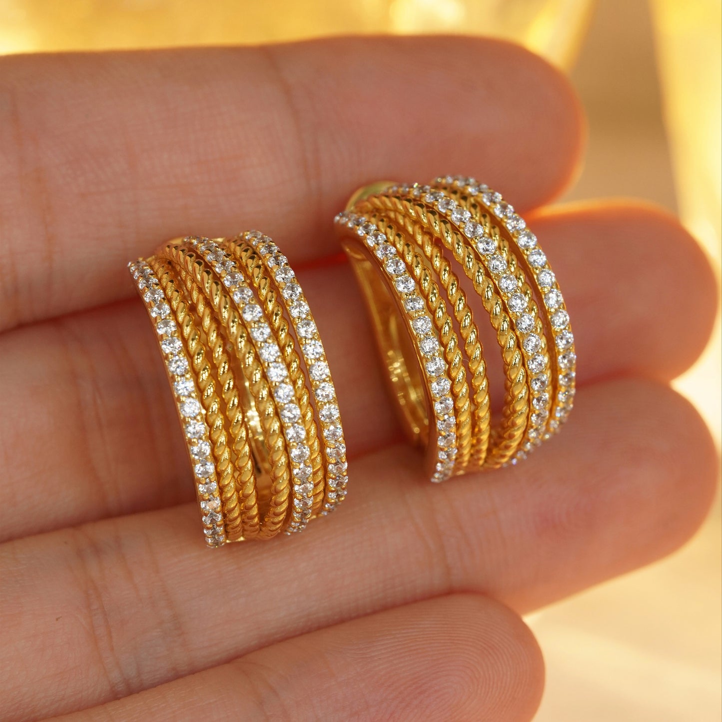 Gold huggie hoop earrings with cubic zirconia worn on hand