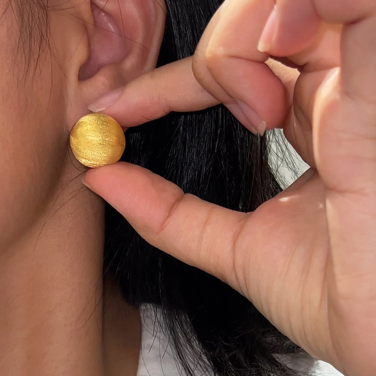 Woman wearing blue CZ reversible huggie earrings with luxury gold finish