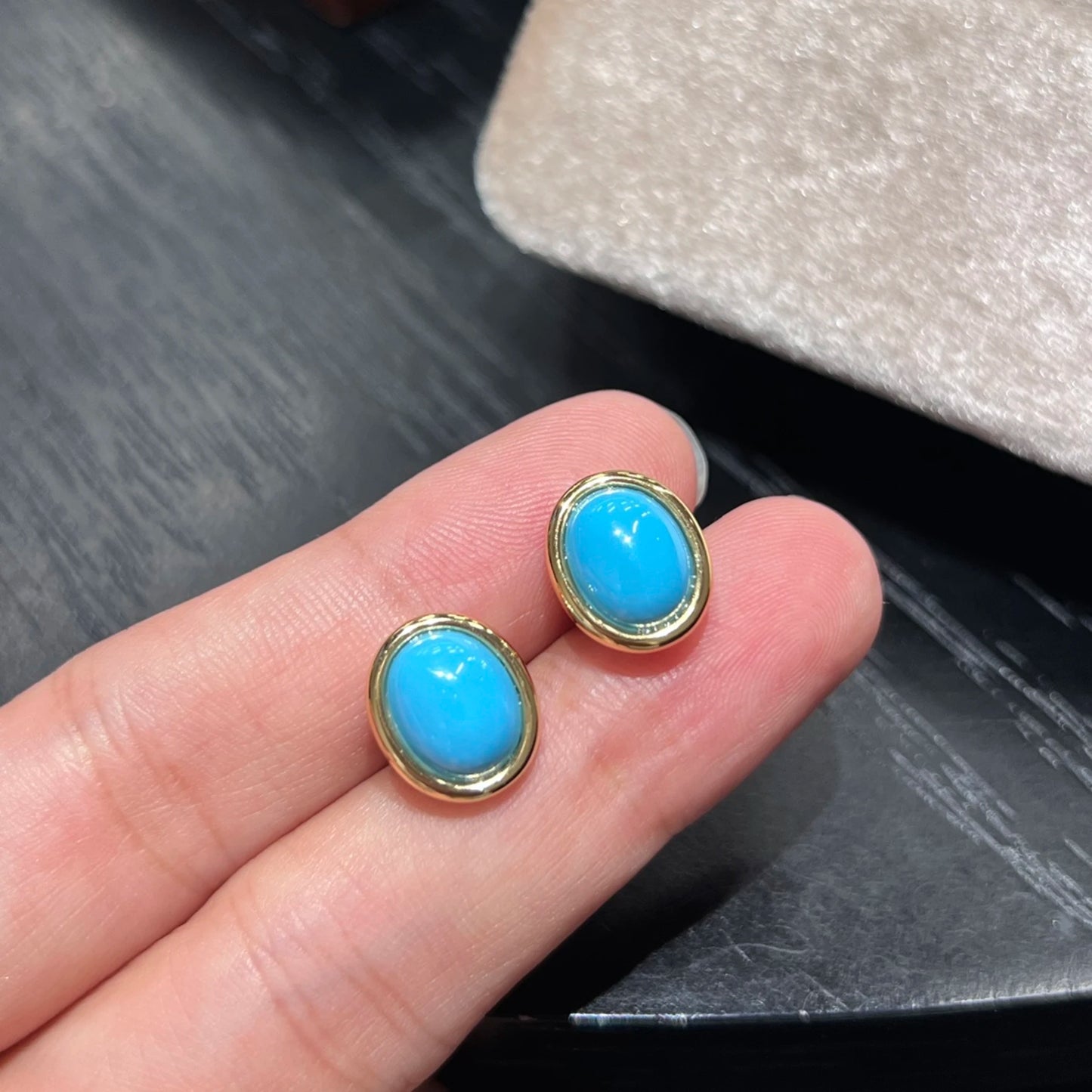 small oval turquoise blue gemstone stud earrings held in hand